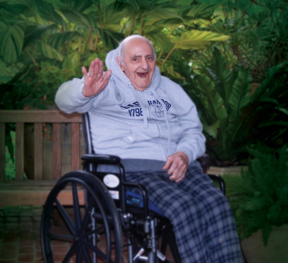 A gentleman waving cheerfully from his wheelchair in the garden