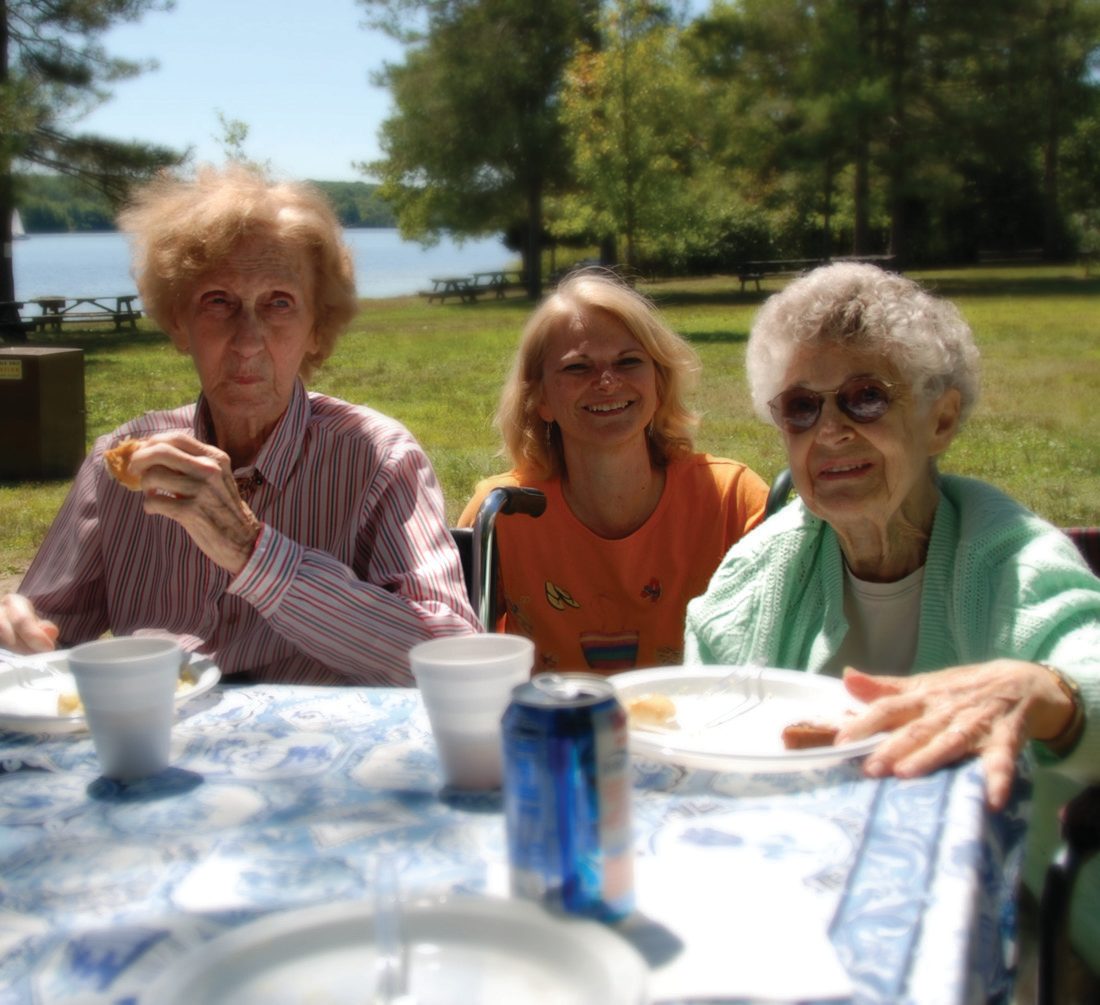 Residents and a caregiver enjoying lunch at a lakeside picnic